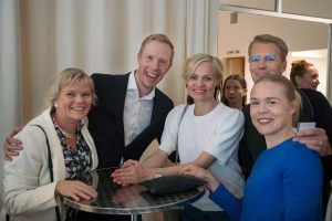 Viisi iloista ihmistä poseeraa hymyillen kameralle pöydän ääressä.