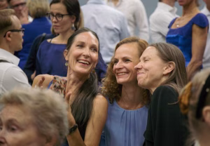 Kolme iloista ihmistä ottamassa selfietä keskellä ryhmäkuvaan valmistautumista.