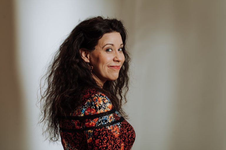 Muotokuva pianisti Anna Laaksosta. Hänellä on tummat, pitkät hiukset ja kukallinen paita.